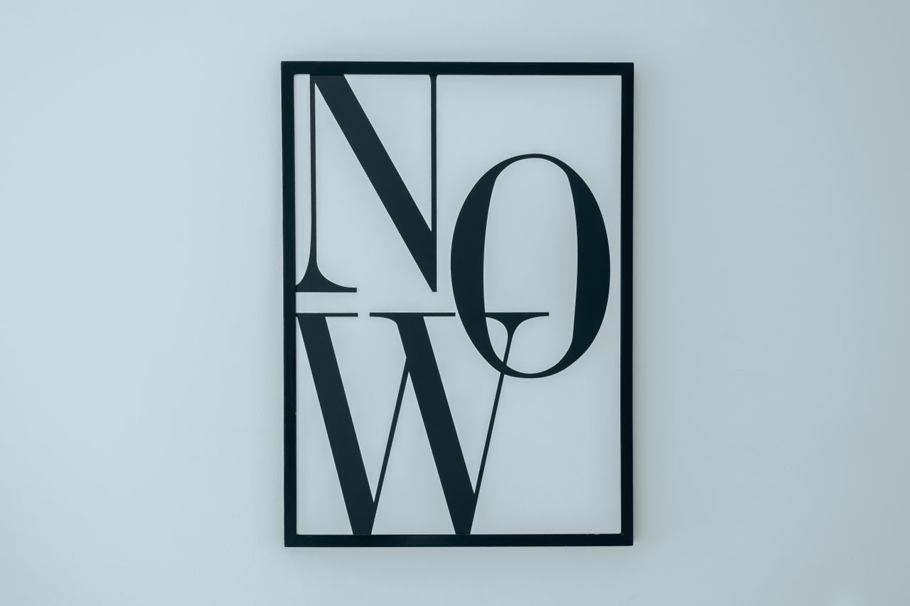 Cadre noir épuré avec le mot NOW sur fond blanc, illustrant un décor minimaliste.